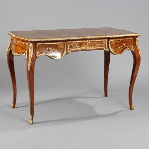 Fritstående skrivebord af rosentræ og nødderod, rigt prydet med monteringer af bronze. Rococoform. 20.-21. årh. H. 80. L. 123. B. 64.