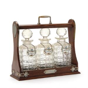 Tantalus af træ med metalmonteringer indeholdende tre karafler af glas. 20. årh. H. 30 cm. L. 33 cm. D. 12,5. cm.