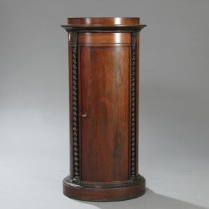 Dansk piedestalskab af palisander, profileret top, front med buet dør, flankeret af snoede søjler med kapitæller. 19. årh.s anden halvdel. H. 142. B. 68. D. 43.