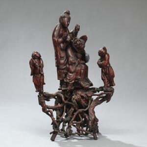 Kinesisk figurgruppe af rigt udskåret rodtræ med dæmon, der serviceres af kvinde og børn. Antageligt 19. årh. H. 75. B. 49 cm.
