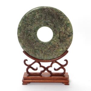 Bi-ring af grønlig sten, skåret med drage der jagter den brændende perle, på stand af træ. H. 38. Diam. 26 cm.
