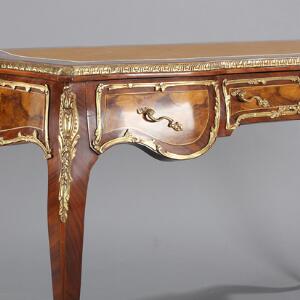 Fritstående skrivebord af rosentræ og nødderod, prydet med beslag af bronze, sarg med tre skuffer. Rococoform. 20.-21. årh. H. 79. L. 124. B. 63.