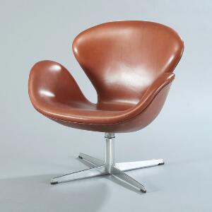 Arne Jacobsen Svanen. Lænestol på helstøbt profileret stamme med firpasfod, skalformet sæde betrukket med brunt skind. Model 3320.