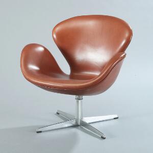 Arne Jacobsen Svanen. Lænestol på helstøbt profileret stamme med firpasfod, skalformet sæde betrukket med brunt skind. Model 3320.