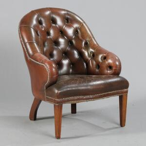 Engelsk lænestol med betræk af brunt skind, dybhæftet ryg og armlæn, ben af mahogni. 19.-20. årh.