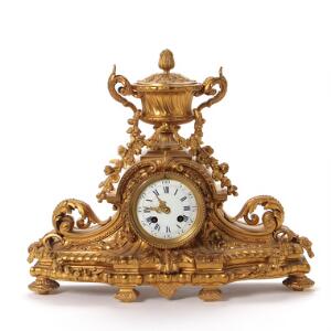 Napoleon III kaminur af forgyldt bronze, støbt med vase, bladværk og guirlander, urskive af hvid emalje prydet med araber og romertal. 19. årh. H. 35 cm.