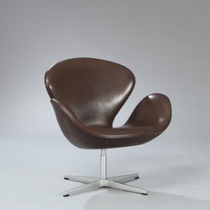 Arne Jacobsen Svanen. Lænestol opsat på stamme med firpasfod af aluminium. Skalformet sæde og ryg betrukket med mørkebrunt skind. Model 3320.