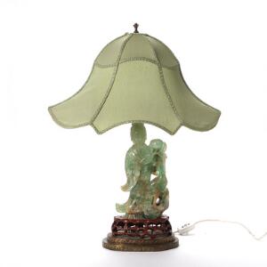 Bordlampe af grøn sten udskåret i form af guanyin med lotusblomst, opstillet på ase af træ og messing. 20. årh. H. 67 cm. figur 30 cm. 