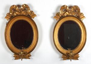 Et par ovale svenske spejllampetter af forgyldt træ, hver med en svungen lysarm af messing. Gustaviansk form, 20. årh. H. 42 cm. 2