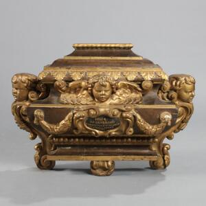 Relikvieskrin af rigt udskåret og delvis bemalet og forgyldt træ, prydet med putti, bladguirlander og perlestaf. Louis XVI. 18. årh. H. 60. B. 80.
