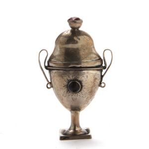 Vaseformet hovedvandsæg, prydet med graveringer og røde flusser. Uidentificeret mester. Med ejerinitialer samt år 1837. H. 8 cm. Vægt 28 gr.