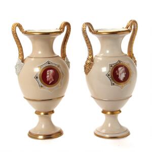 To prydvaser af porcelæn, dekorerede i guld og lysbeige, hanke i form af horn og satyrhoveder i relief. Danmark, 19. årh. H. 34 cm. 2
