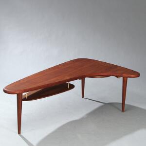 Ubekendt designer Sofabord af teak, opsat på tre tilspidsende ben. Organisk formet plade, under hvilken hylde samt udtræksbakke med sort formika.