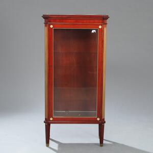 Vitrine af mahogny, med ornamenter af bronze samt dør flankeret af kanneleringer. Louis XVI stil, 20. årh. H. 137. B. 62. D. 34.