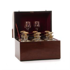 Flaskeskrin af mahogni hvori seks seks firsidede karafler af glas samt to glas dekorerede med guld. 19. årh. Skrin H. 21 cm. B. 27 cm. D. 19 cm.
