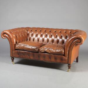 To-personers Chesterfield sofa, ryg, sider og løse hynder med lyst brunt læder, drejede forben af mahogni med messinghjul. 20. årh. L. 190.