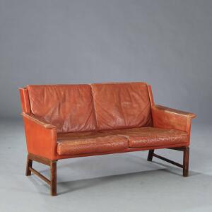 Kaj Lyngfeldt Larsen Fritstående to-pers. sofa, opsat på ben af palisander. Sider, armlæn samt løse hynder betrukket med rød-brunt farvet skind.