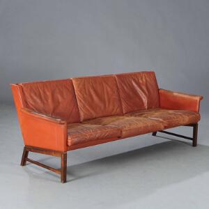 Kaj Lyngfeldt Larsen Fritstående tre-pers. sofa, opsat på ben af palisander. Sider, armlæn samt løse hynder betrukket med rød-brunt farvet skind.