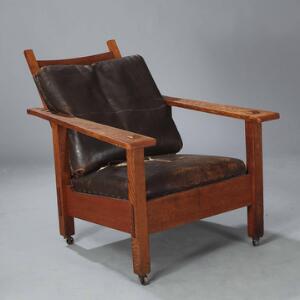 Morris chair. Armstol af patineret eg, med justerbar ryg. Opsat på hjul. Løse hynder i sæde samt ryg betrukket med brun skind.