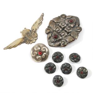 Skønvirke bæltespænde, broche og seks knapper af sølv, prydet med cabochonslebne granater samt logo af sølv. L. 1,8-9. 9