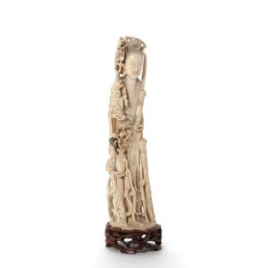 Stående Guyanyin af elfenben, udskåret med bånd og personer, en med krukke med frugtgrene. Kina 19.20. årh. Med stand af træ. H. uden stand 29 cm.