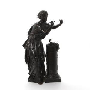 Figur af patineret bronze i form af muse i klassiske gevandter stående ved søjle med inskription af digternavne. 19. årh. H. 44 cm.