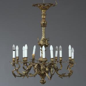 Nyrokoko lysekrone af bronze og messingblek med 12 svungne lysarme, monteret til el. 19. årh.s slutning. H. 105. Diam. 92.
