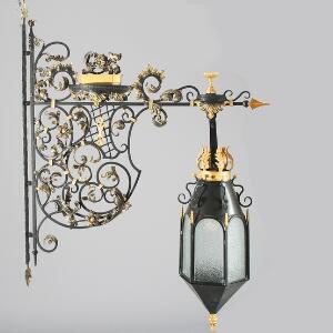 Udendørs væglampe af sort- og guldmalet jern, støbt med ornamentik, blomster og bladværk, sekssidet lanterne med glas. H. 160. B. 121.