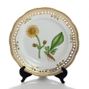 Flora Danica. Gennembrudt tallerken af porcelæn dekoreret i farver og guld med blomst. Kgl. P. nr. 3553. Diam. 25,5 cm.