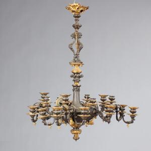 Lysekrone af delvis forgyldt og patineret bronze med 20 lysarme, prydet med masker, løvehoveder, bladværk og ornamentik. 19. årh. H. 80. Diam. 68.