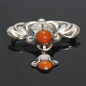 Skønvirkebroche af sølv prydet med abochonslebet rav. L. ca. 6 cm. Ca. 1920-30.