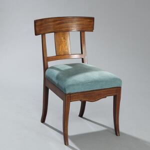 Dansk senempire stol af mahogni indlagt med lyst træ, buet rygstykke indlagt med klassisk figur, let svejede ben. 19. årh.s begyndelse.