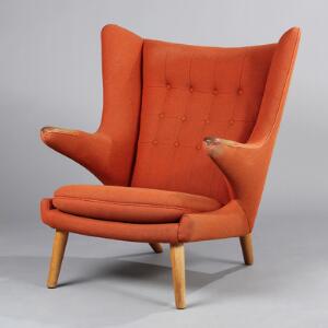 Hans J. Wegner Bamsestol. Øreklapstol med ben og negle af eg, betrukket med orangerødt uld. Udført hos AP-Stolen.