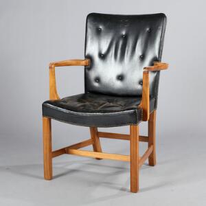 Palle Suenson Armstol af nøddetræ betrukket i sæde og ryg med sort dybthæftet skind, beslået med messingsøm. Udført hos Jacob Kjær.