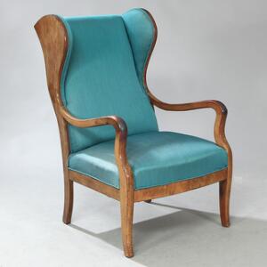 Frits Henningsen Øreklapstol med stel af mahogni. Sæde samt ryg betrukket med blågrønt stof. Udført hos snedkermester Frits Henningsen.