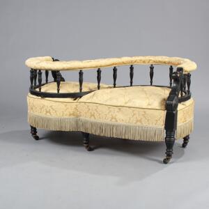 Engelsk tête-à-tête sofa af sortlakeret træ, betrukket med lyst brokadestof med frynser. Ca. 1900. L. 130.