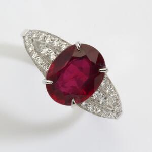Rubin- og diamantring af 18 kt. hvidguld prydet med oval facetslebet rubin omkranset og flankeret af talrige brillant- og baguetteslebne diamanter.