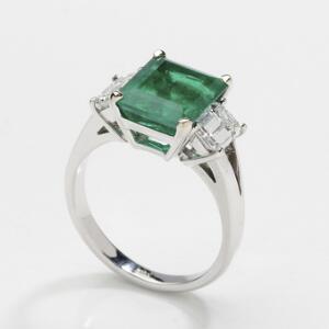 Smaragd- og diamantring af 18 kt. hvidguld prydet med smaragdslebet smaragd på ca. 4.00 ct flankeret af to smaragdslebne diamanter på i alt ca. 1.20 ct. Str. 52