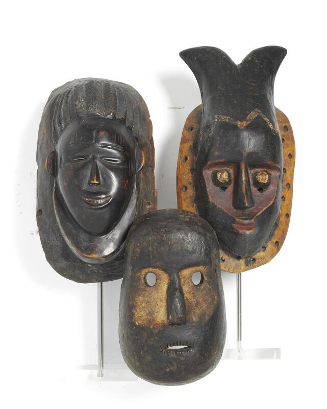 Three masks of carved patinated wood with traces of red, white and black...
